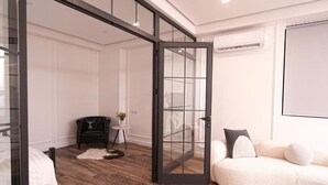 A modern room with a glass door leading to a balcony, a white sofa, a small round table with a vase, and a leather chair.