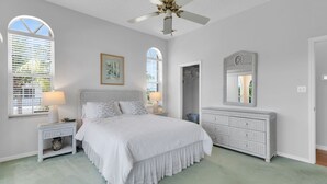 Ein Schlafzimmer mit Bett, Kommode, Deckenventilator und einem Fenster mit Jalousien.