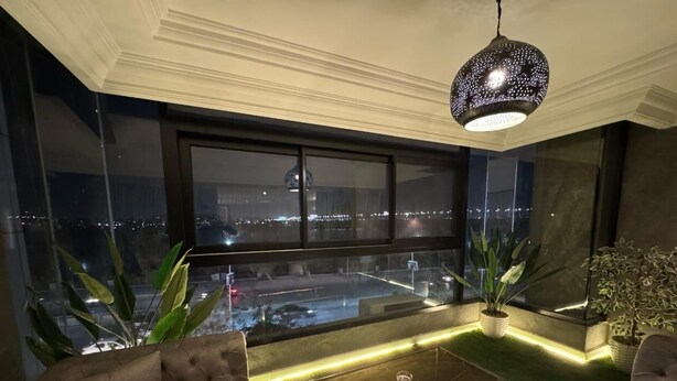A modern living room with a large window, a tufted sofa, a glass coffee table, and a decorative hanging light fixture.