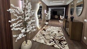 A modern hallway with a large mirror, a white artificial tree, and a patterned rug.
