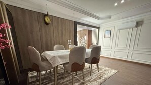 A dining area with a wooden table and chairs, a patterned rug, and a clock on the wall.