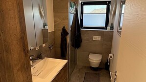 Un bagno moderno con un mobile bagno in legno, un WC e una doccia.