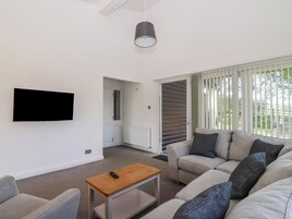 Una sala de estar moderna con un televisor de pantalla plana, una mesa de centro de madera y un sofá con varios cojines.