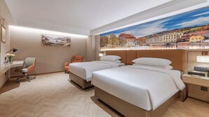 Een hotelkamer met twee bedden, een bureau, een stoel en een groot raam met uitzicht op de stad.