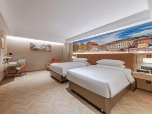 Ein Hotelzimmer mit zwei Betten, einem Schreibtisch, einem Stuhl und einem großen Fenster mit Blick auf die Stadt.