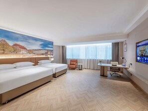 Une chambre d’hôtel avec deux lits, un bureau, une chaise, une télévision et une grande fenêtre avec des rideaux.