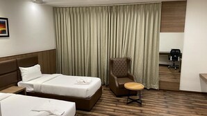 Ett hotellrum med två sängar, en stol, ett litet bord, ett skrivbord och en kaffemaskin.
