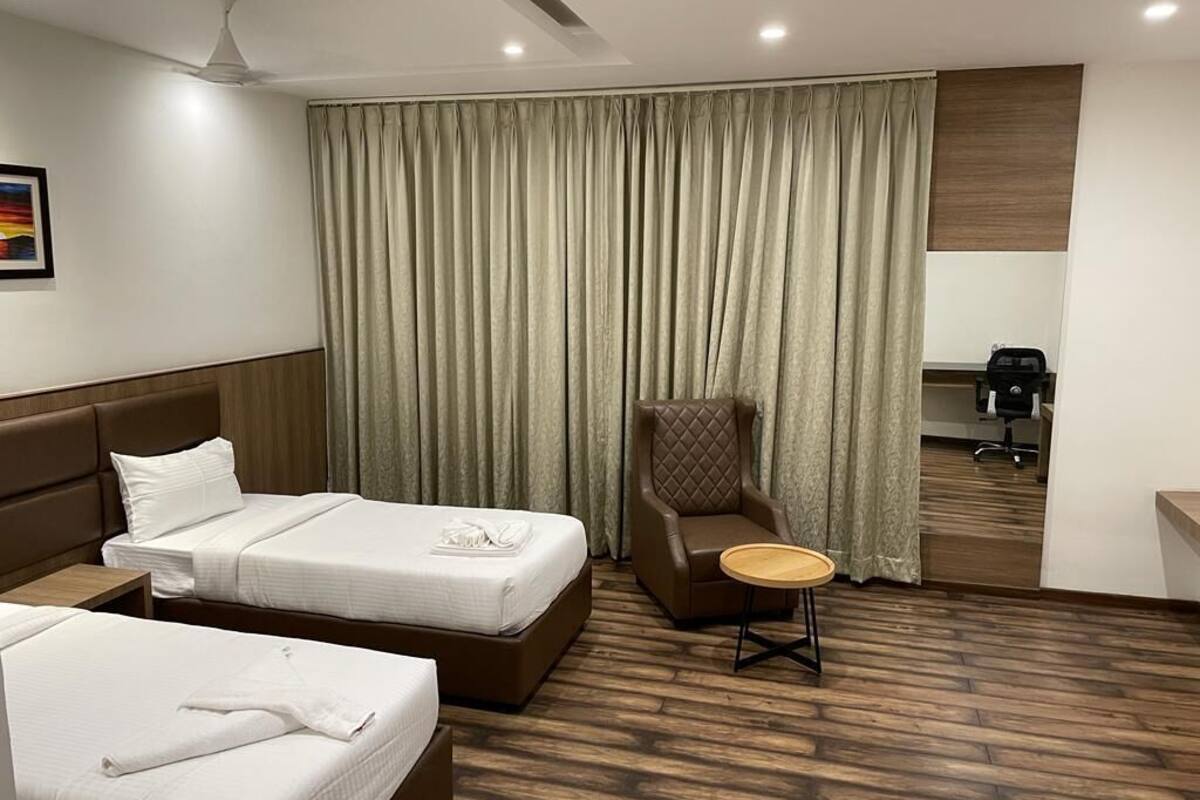 A hotel room with two beds, a chair, a small table, a desk, and a coffee machine.