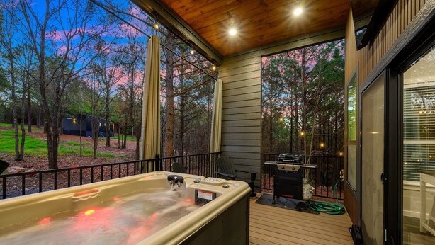 Een hottub op een houten terras, met uitzicht op bomen en een barbecueplaats.