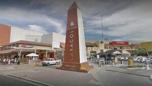 Una plaza con un monumento destacado, una gasolinera y algunos edificios con letreros.