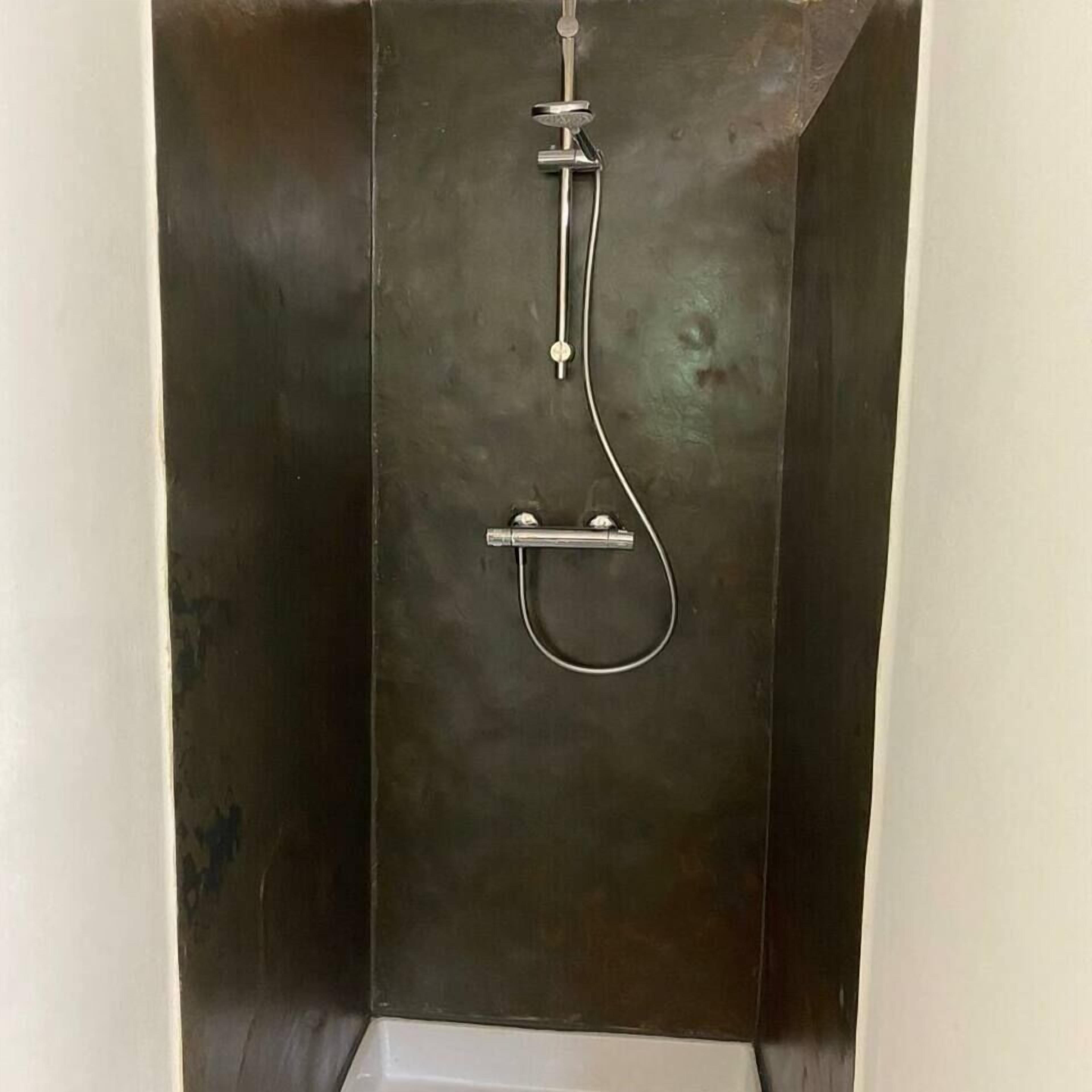 A metallic, industrial-style shower enclosure with a handheld showerhead and a fixed faucet.