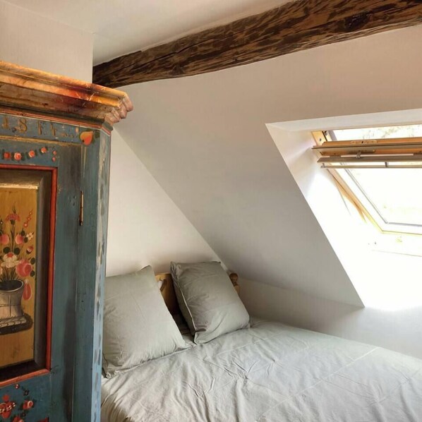 A bedroom with a sloped ceiling, a skylight, and a bed with pillows.