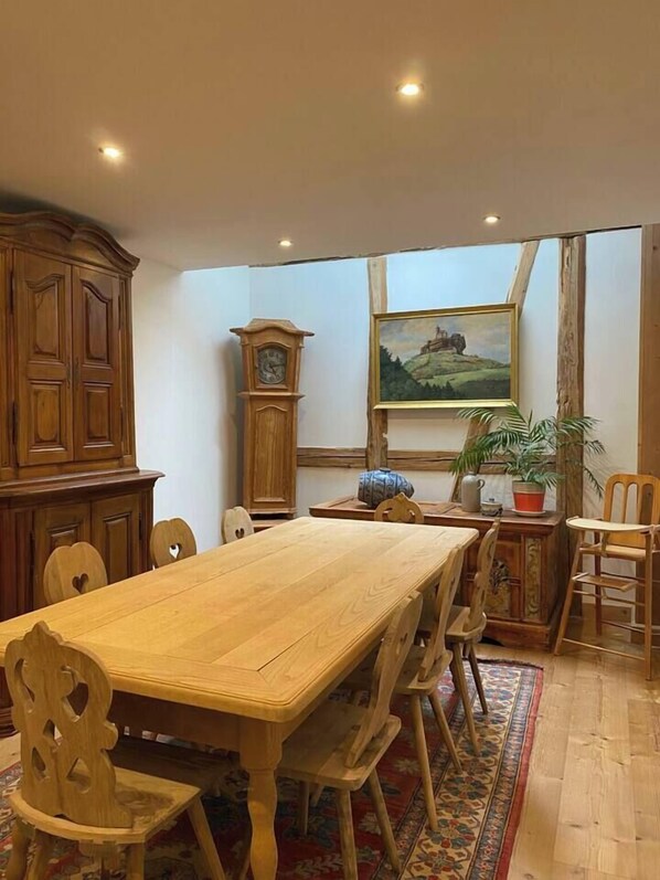 Un comedor con una mesa y sillas de madera, un reloj, un cuadro y una planta en maceta.