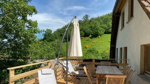 A wooden deck with a table and chairs, a sun umbrella, and a view of a green landscape.