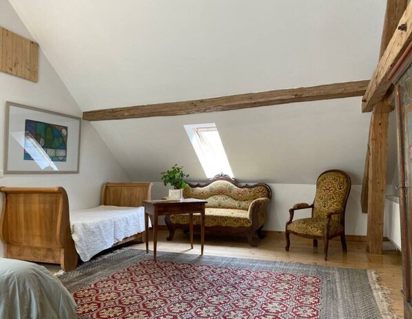 Un dormitorio cálido en el ático con techo inclinado, una cama de madera, un sofá, una silla y una mesita.
