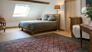 A bedroom with a sloped ceiling, a bed, a floor lamp, a wooden chair, a small table, and a potted plant.