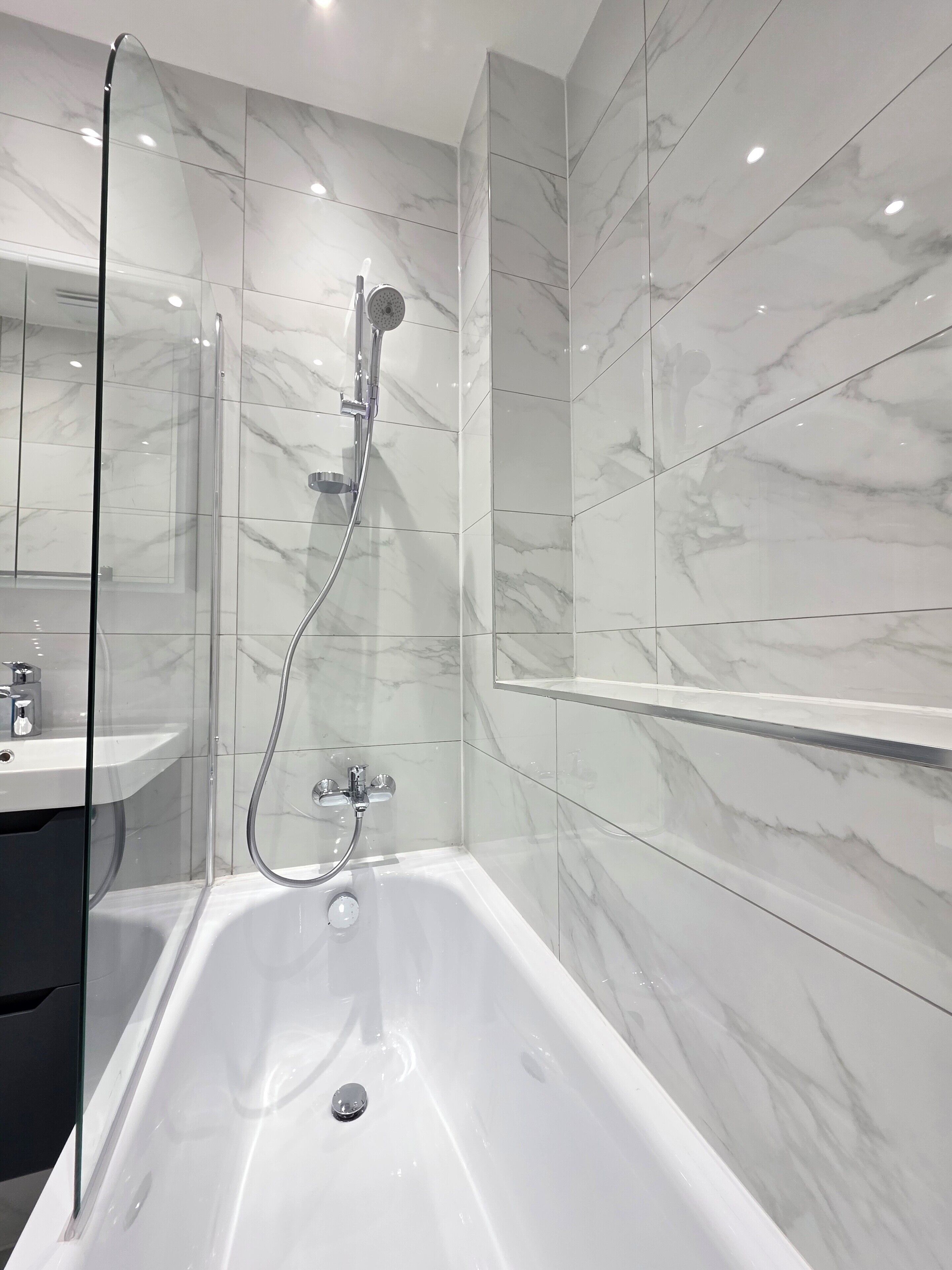 Un baño moderno con ducha de vidrio, una bañera blanca y paredes cubiertas de mármol.