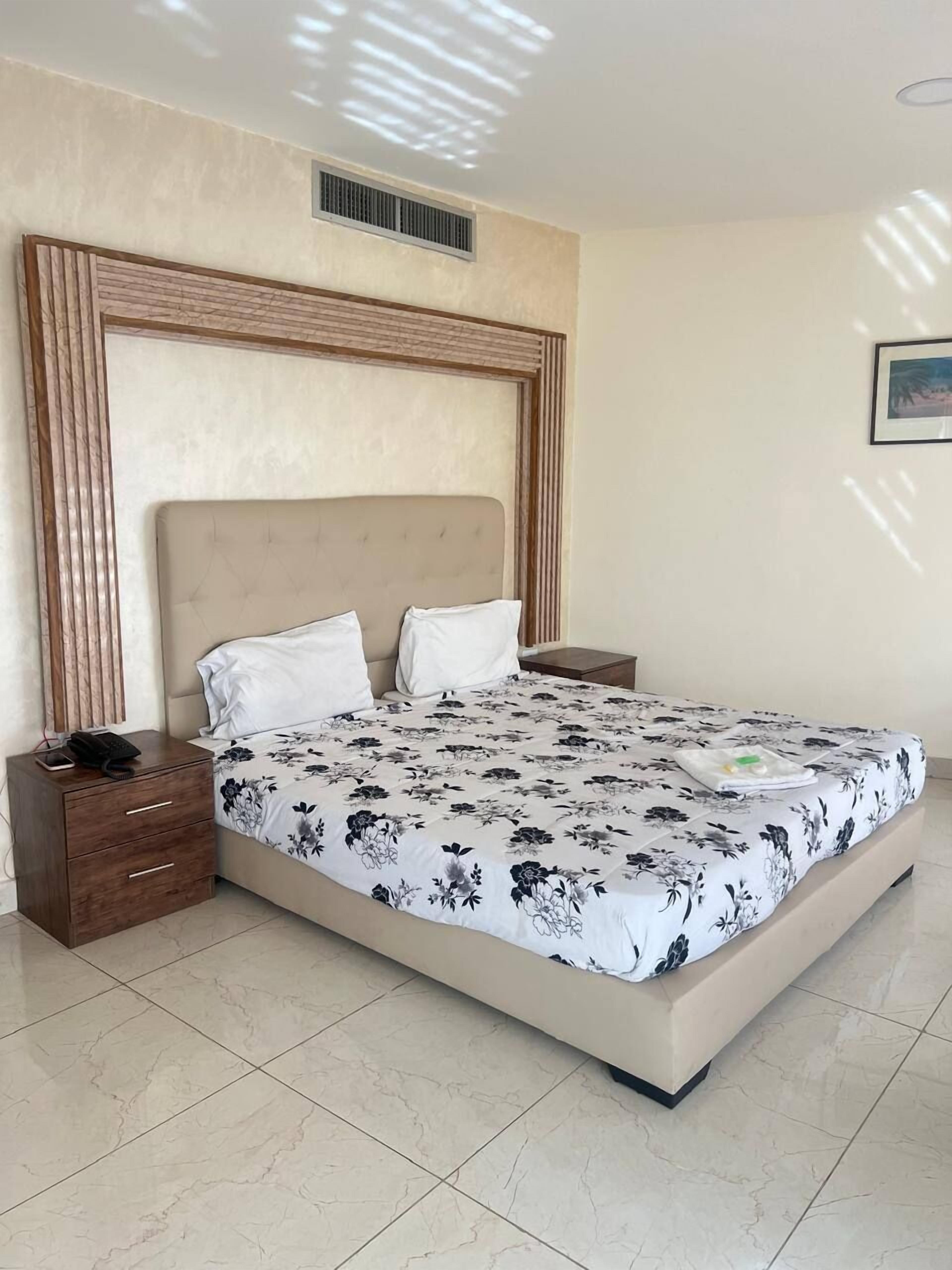 A bedroom with a large bed, a nightstand, a wooden headboard, and a framed picture on the wall.