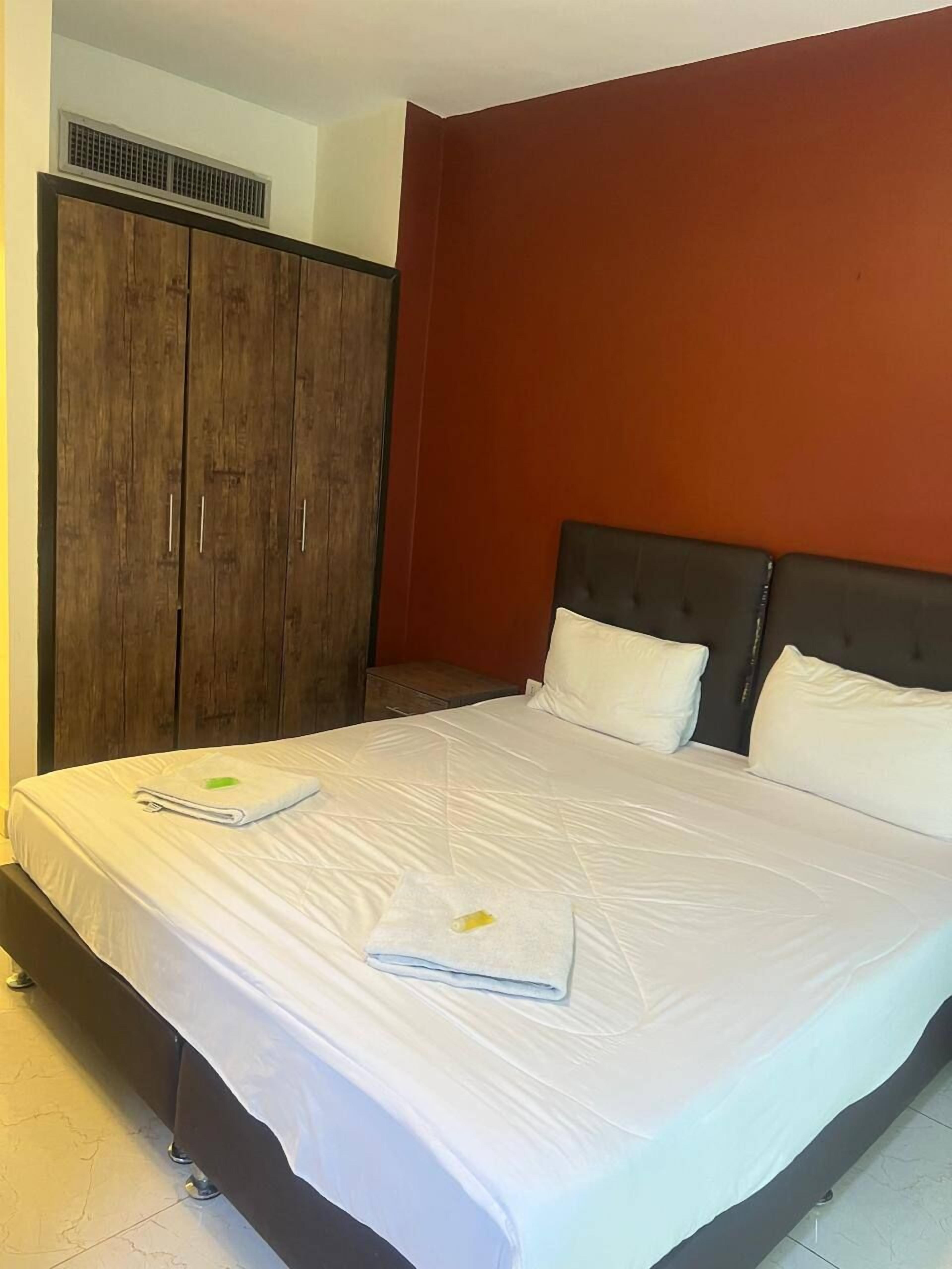 A hotel room with a large bed, a wardrobe, and a red accent wall.