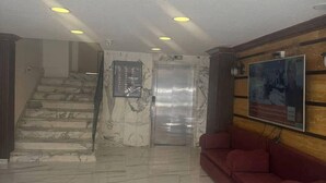 A lobby with marble flooring, a staircase, a red sofa, and an elevator. - Larnaka Hotel (Amman)