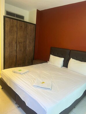A hotel room with a large bed, a wardrobe, and a red accent wall. - Larnaka Hotel (Amman)
