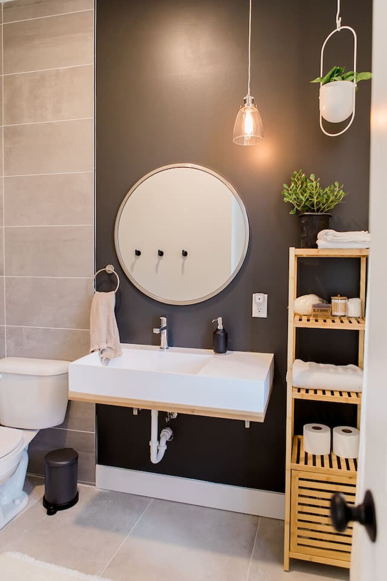 A modern bathroom with a round mirror, white sink, and a wooden shelf with toiletries.