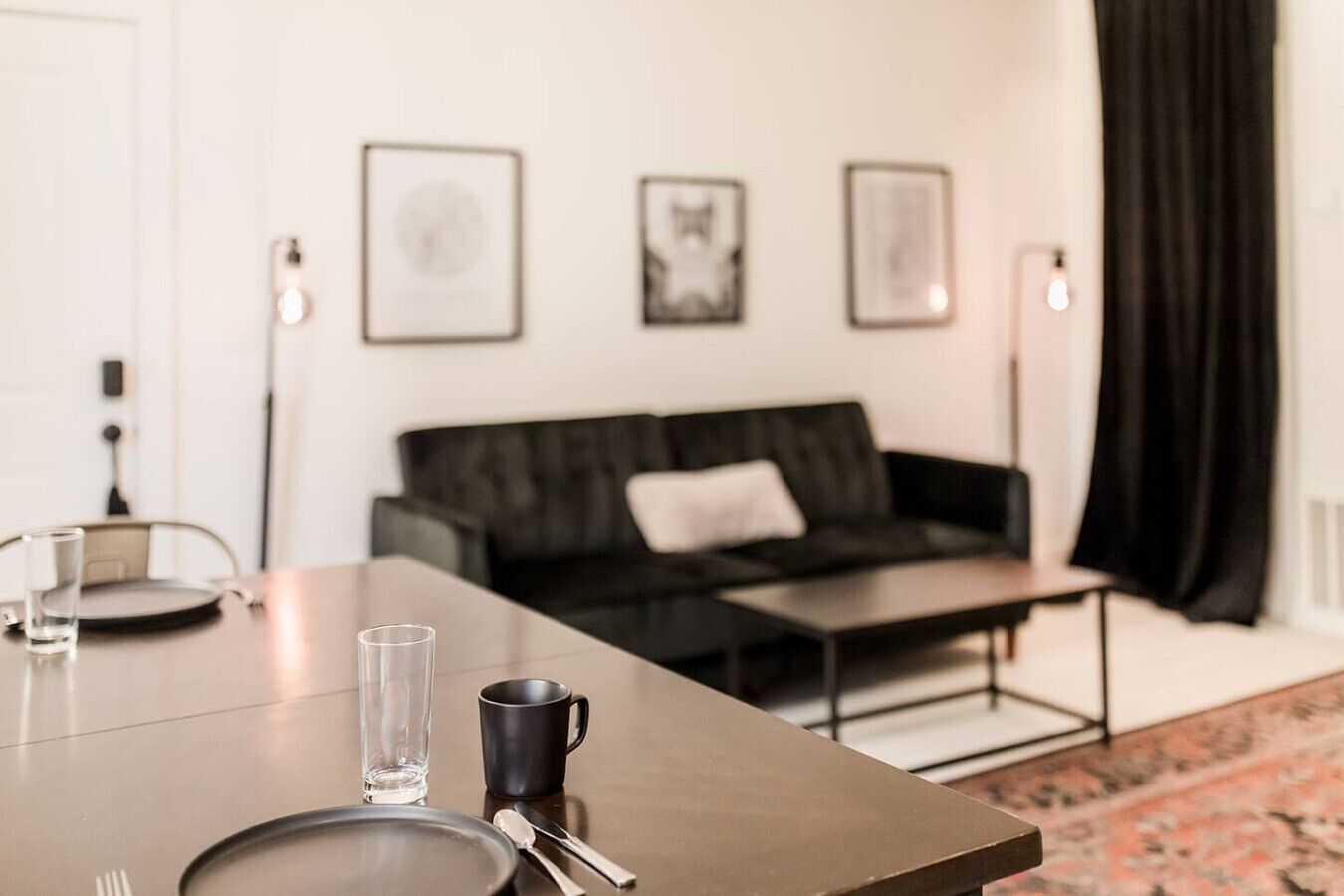 A modern living room with a dark sofa, a coffee table, and a dining table set with cutlery and a glass.