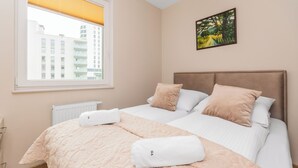 Une chambre d’hôtel avec deux lits, une fenêtre avec des stores, un radiateur et un tableau au mur.