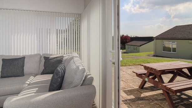Een moderne woonkamer met een bank en een schuifdeur die leidt naar een terras met een houten tafel en bankjes.