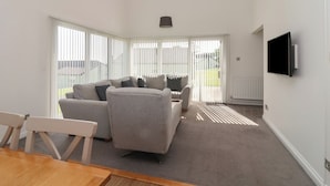 Een moderne woonkamer met een grijze bank, een houten eettafel en een aan de muur bevestigde televisie.