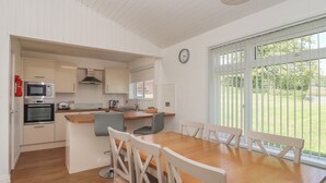 Een moderne keuken met inbouwapparatuur, een eethoek met een houten tafel en witte stoelen, en een groot raam met uitzicht op een groen landschap.