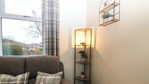 A living room with a brown sofa, plaid cushions, a small white table, and a floor lamp. - 60E Wellgate (Lanark)