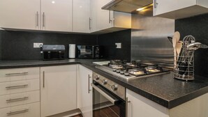 A modern kitchen with white cabinets, a stainless steel range hood, a gas stove, and a microwave. - 60E Wellgate (Lanark)