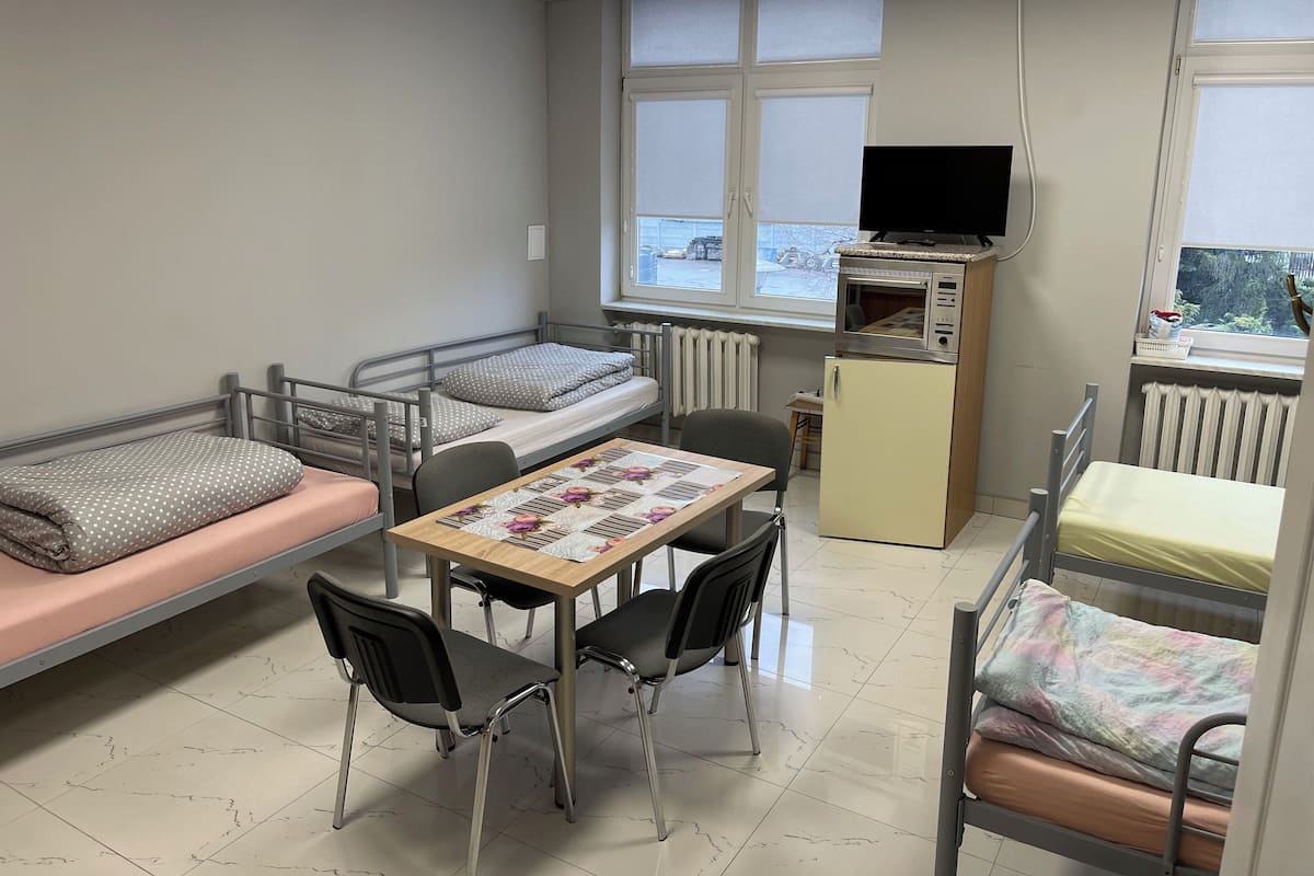 Habitación tipo dormitorio con dos camas individuales, una mesita con sillas, un televisor y un refrigerador.