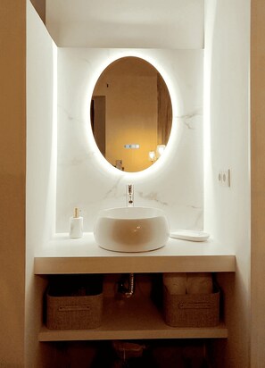 A bathroom with a round mirror, a white sink, and two storage baskets.