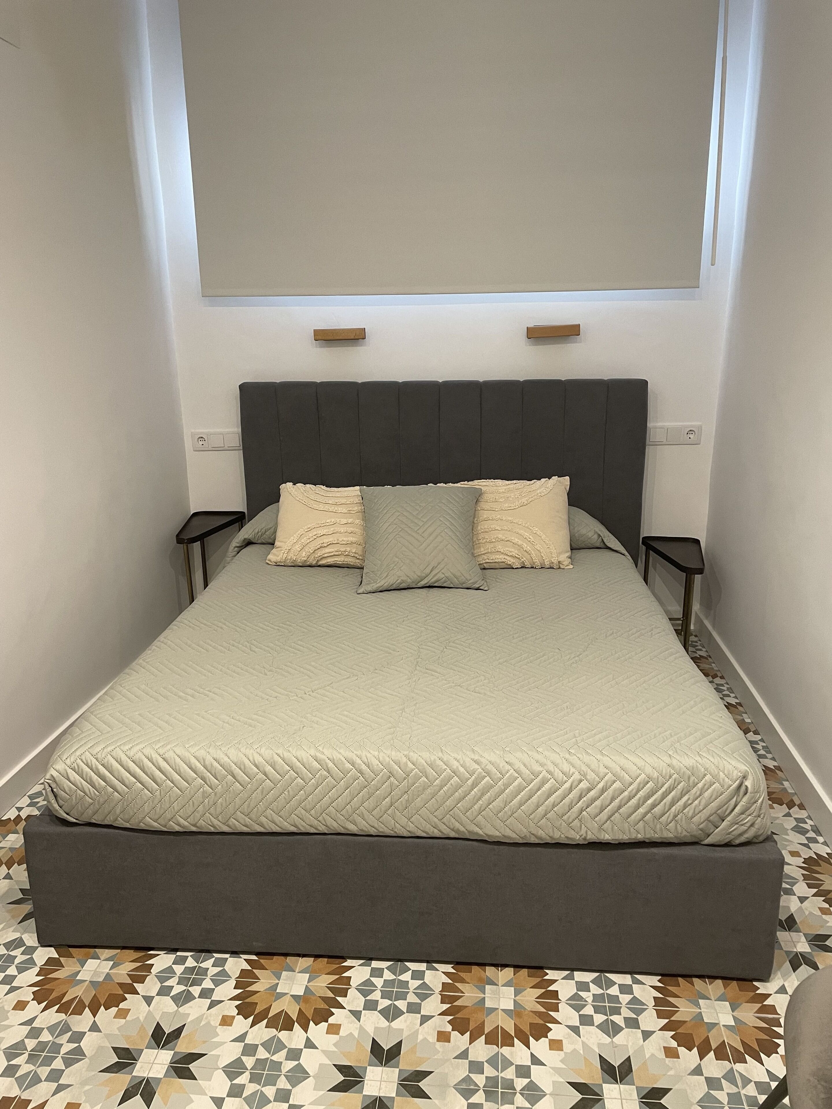 Ein Schlafzimmer mit einem Bett, zwei Nachttischen, einem Kopfteil und einem gemusterten Boden.