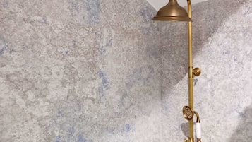 A shower with a gold-colored showerhead and controls mounted on a wall.