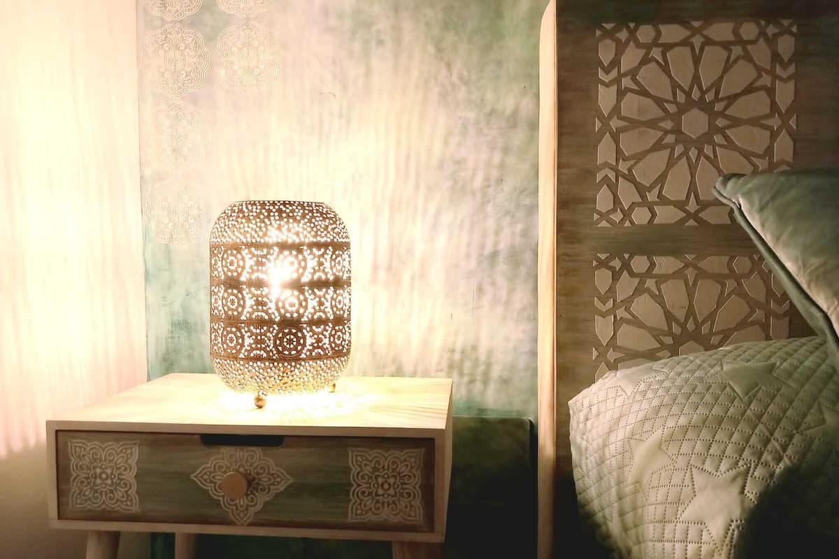 Une table de chevet avec une lampe à motifs, un lit avec une tête de lit à motifs géométriques et un mur avec un motif texturé.