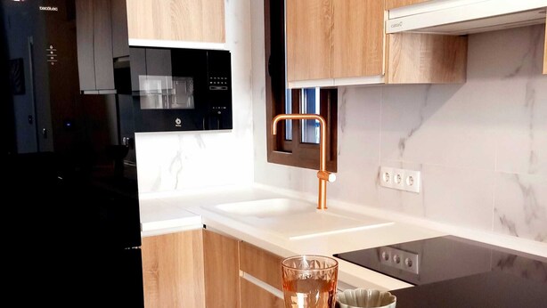 Une cuisine moderne avec un plan de travail noir, une assiette ronde de couleur beige, un verre de thé glacé, une cuillère et une fourchette.