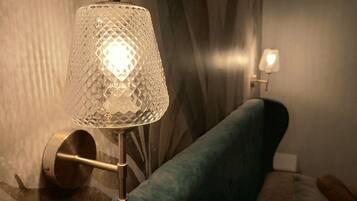 A lamp with a textured glass shade on a stand, positioned next to a sofa with a patterned cushion.