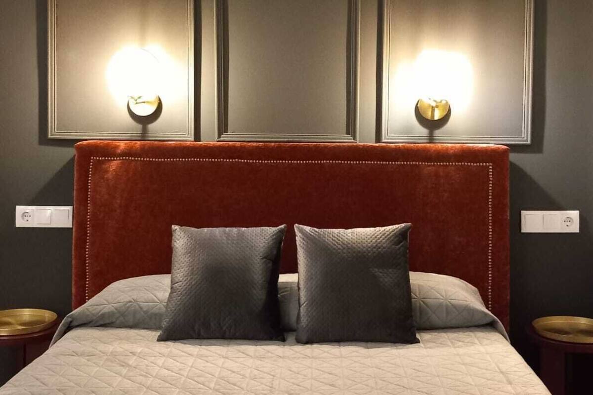 Un lit bien fait, avec une couverture matelassée, une tête de lit en bois et deux lampes fixées au mur.