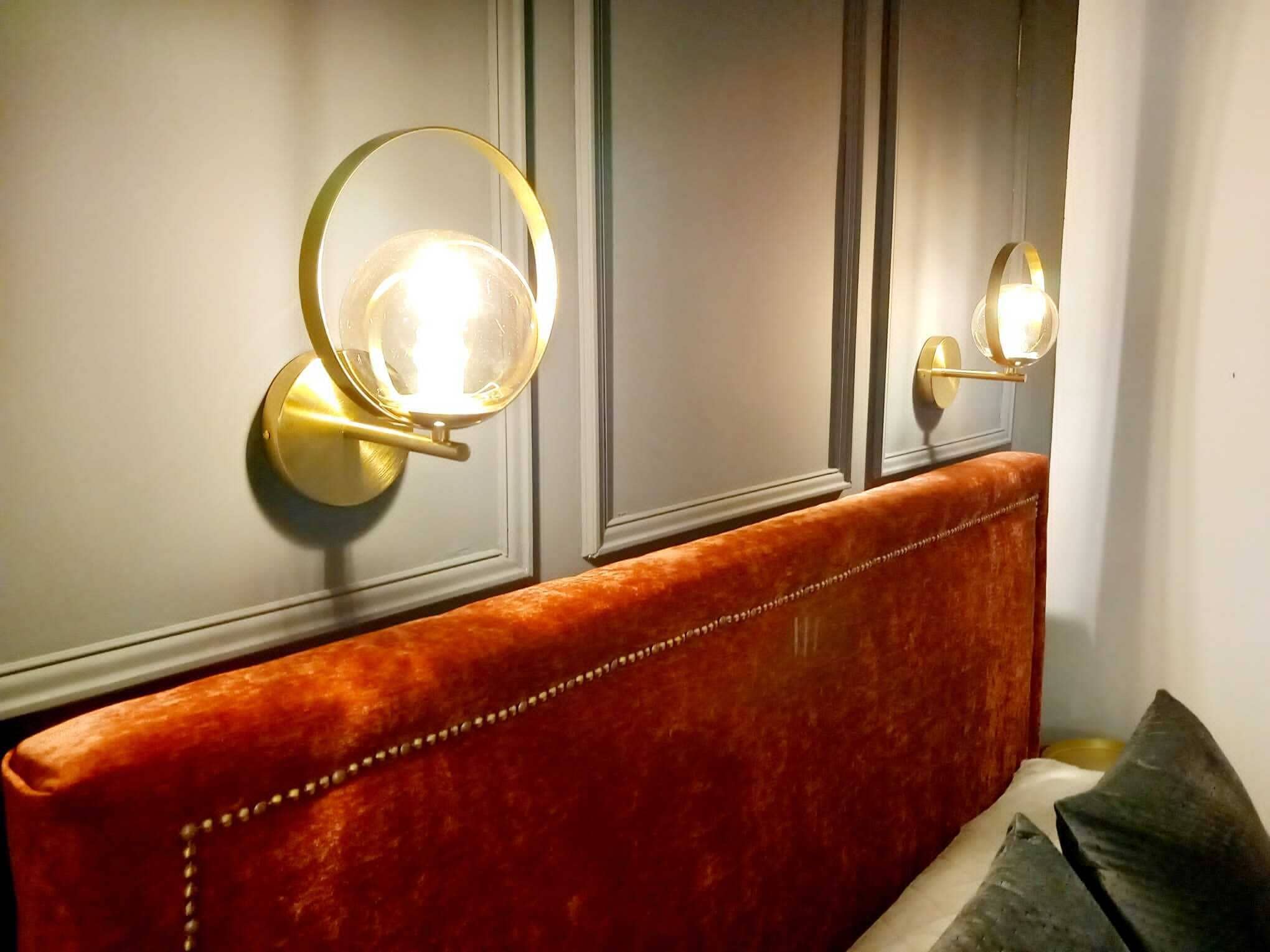 A room with a red upholstered headboard, a wall-mounted light fixture, and a door with a golden handle.
