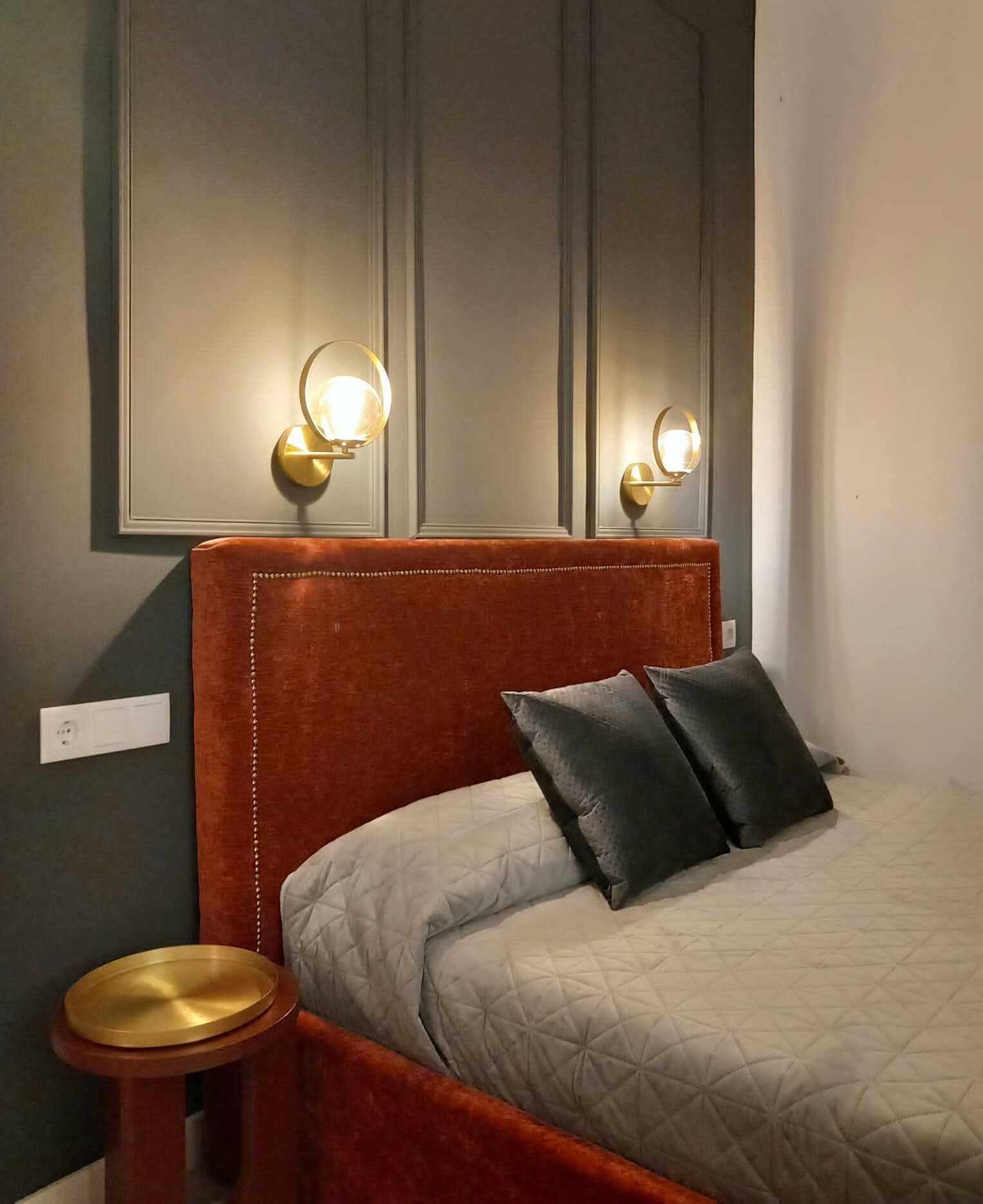 Una cama con cabecera roja, dos almohadas y una mesita de noche con una lámpara.