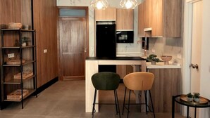 Une cuisine moderne avec des meubles en bois, un plan de travail noir et deux chaises. Une petite table ronde, ornée de plantes, se trouve sur la droite.
