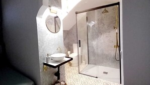 Une salle de bain moderne avec un lavabo sur pied, un miroir rond, une douche avec une porte en verre et des carreaux de sol à motifs.