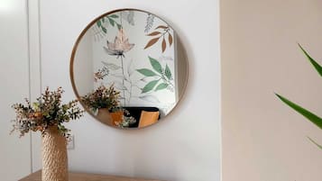 A round mirror with a floral design on a wall, a wooden table with a vase of dried flowers, and a potted plant.