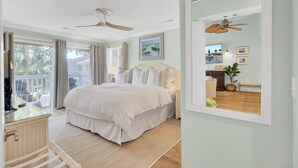 Ein Schlafzimmer mit Bett, Deckenventilator, großem Fenster und Ausblick nach draußen.