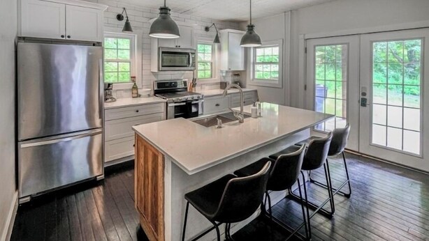 A modern kitchen with stainless steel appliances, a large island with bar stools, and large windows providing natural light. - Large Farmhouse Steps from Downtown Ludlow & Okemo Shuttle (Ludlow)