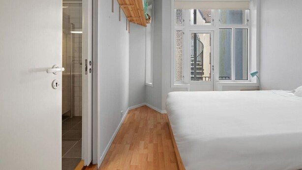 Ein Schlafzimmer mit Holzboden, einem Bett, einem Fenster mit Aussicht und einer Tür zu einem Badezimmer.