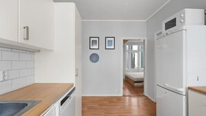 Eine moderne Küche mit weißen Schränken, einer Holzarbeitsplatte und einem eingebauten Geschirrspüler. An der Wand hängen zwei gerahmte Bilder und darüber befindet sich eine Mikrowelle.